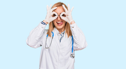 Beautiful caucasian woman wearing doctor uniform and stethoscope doing ok gesture like binoculars sticking tongue out, eyes looking through fingers. crazy expression.