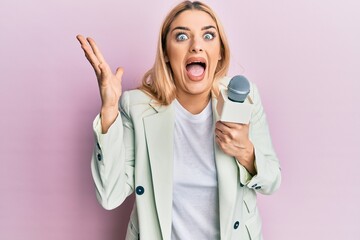 Young caucasian woman holding reporter microphone celebrating victory with happy smile and winner...