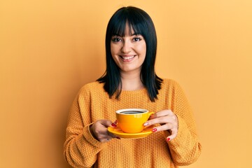 Young hispanic woman holding coffee smiling with a happy and cool smile on face. showing teeth.