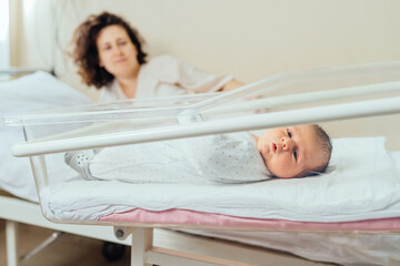 Beautiful newborn baby boy, laying in crib, wake up his mother in prenatal hospital.