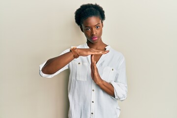 Young african american girl wearing casual clothes doing time out gesture with hands, frustrated...