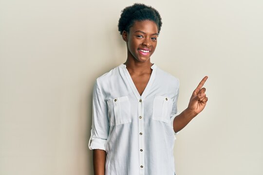 Young african american girl wearing casual clothes with a big smile on face, pointing with hand finger to the side looking at the camera.