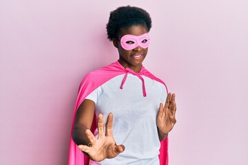 Young african american girl wearing superhero mask and cape costume disgusted expression, displeased and fearful doing disgust face because aversion reaction. with hands raised
