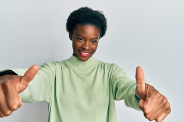Young african american girl wearing casual clothes approving doing positive gesture with hand, thumbs up smiling and happy for success. winner gesture.