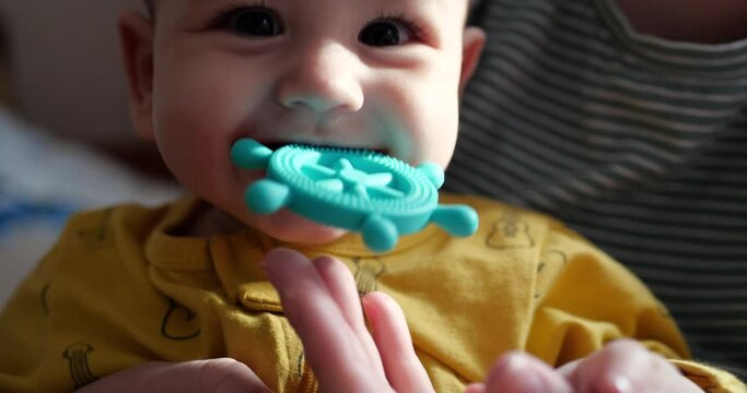 A young mother sits on the bed with a small child in her arms and controls the game with a teether and other tactile toys. Maternity, motherhood and family concept. slow motion
