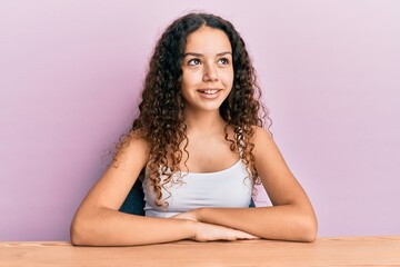 Obraz na płótnie Canvas Teenager hispanic girl wearing casual clothes sitting on the table looking to side, relax profile pose with natural face and confident smile.