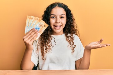 Teenager hispanic girl holding swiss franc banknotes celebrating achievement with happy smile and winner expression with raised hand