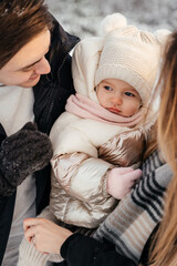 Young parernts holding small daughter in winter forest