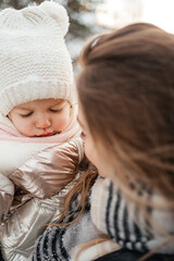 Young mom holding sad, small beautiful baby girl in winter hat