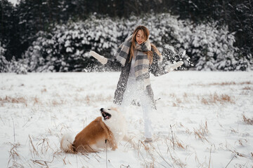 Young blonde hair girl playing with akita dog in winter forest
