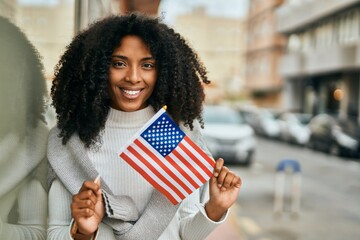 Young african american woman smiling happy holding United States flag at the city.