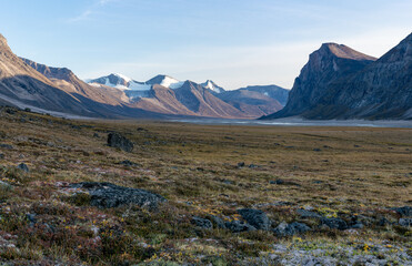 Monumental, wild arctic valley during sunset. Tall peaks with snow on top and river bed below. Duskfall at Akshayuk pass, Baffin Island, Canada.