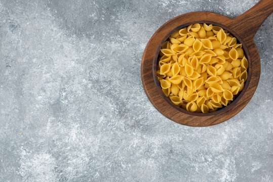 Wooden bowl of raw seashell pasta on cutting board
