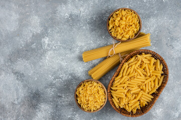 Pile of various uncooked dry pasta in wicker basket and wooden bowls