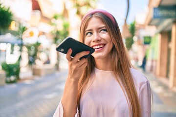 Young caucasian girl smiling happy sending audio message using smartphone at the city.