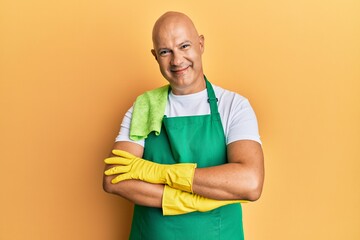 Middle age bald man wearing apron holding cleaning gloves happy face smiling with crossed arms looking at the camera. positive person.