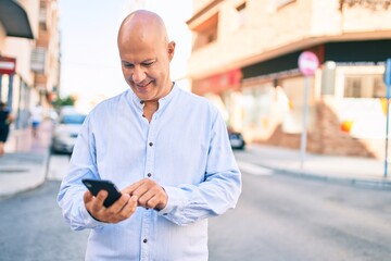 Middle age bald man smiling happy using smartphone at the city.
