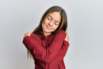 Beautiful brunette little girl wearing casual sweater hugging oneself happy and positive, smiling confident. self love and self care