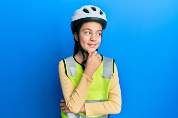 Beautiful brunette little girl wearing bike helmet and reflective vest with hand on chin thinking about question, pensive expression. smiling with thoughtful face. doubt concept.