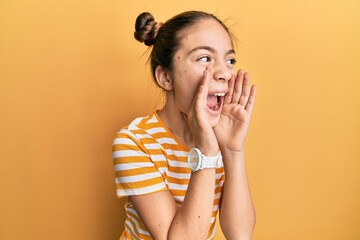 Beautiful brunette little girl wearing casual striped t shirt shouting angry out loud with hands over mouth