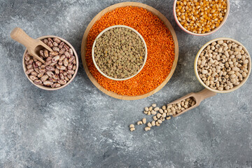 Colorful bowls of various uncooked beans, lentils and corns on marble surface
