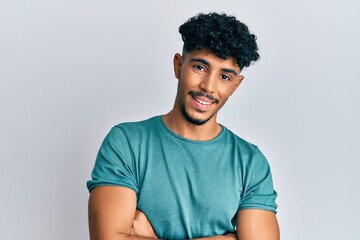 Young arab handsome man wearing casual clothes happy face smiling with crossed arms looking at the...