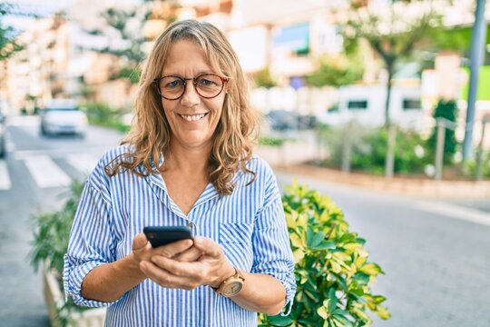 Middle age caucasian woman smiling happy using smartphone at the city.