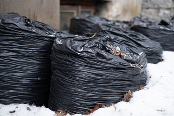 Black plastic trash bags filled with garbage waiting for removal. Trash bags on a side of a house during winter.