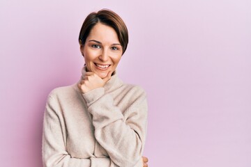 Fototapeta premium Young brunette woman with short hair wearing casual winter sweater looking confident at the camera smiling with crossed arms and hand raised on chin. thinking positive.