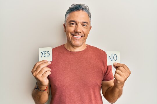 Handsome Middle Age Mature Man Holding Yes And No Reminder Smiling With A Happy And Cool Smile On Face. Showing Teeth.