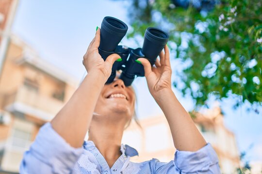 Young blonde woman smiling happy looking for new opportunity using binoculars at the park,