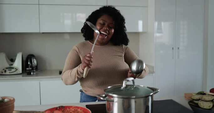 Young curvy latin woman having fun cooking and dacing inside kitchen at home 