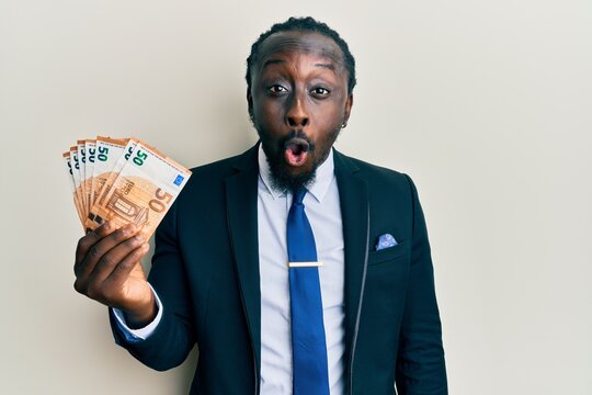 Handsome young black man wearing business suit holding 50 euros banknotes scared and amazed with open mouth for surprise, disbelief face