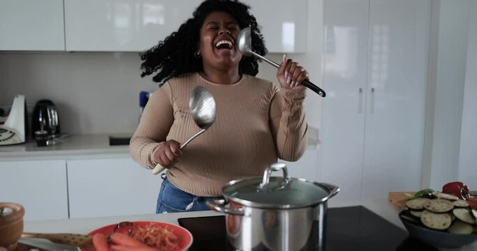 Young curvy latin woman having fun cooking and dacing inside kitchen at home 