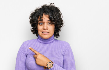 Young hispanic woman with curly hair wearing casual clothes pointing aside worried and nervous with forefinger, concerned and surprised expression