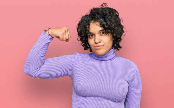Young hispanic woman with curly hair wearing casual clothes strong person showing arm muscle, confident and proud of power