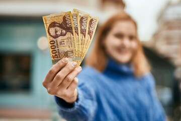 Young caucasian girl smiling happy holding hungarian forint banknotes at the city.