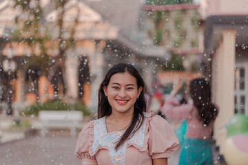 portrait of smiling happy Asian woman looking at camera with snow falling around in town, snowy day, happy winter