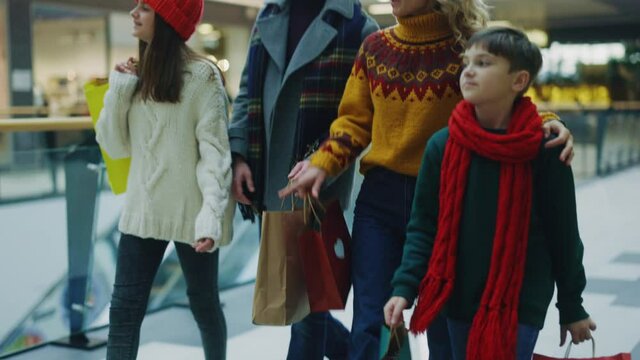 Pleased young family of married couple parents and their adorable children walking at shopping mall enjoying each other company. Shopping bags. Christmas. Winter.