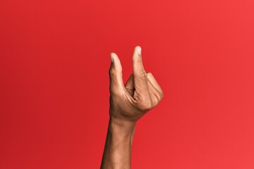 Hand of hispanic man over red isolated background picking and taking invisible thing, holding object with fingers showing space