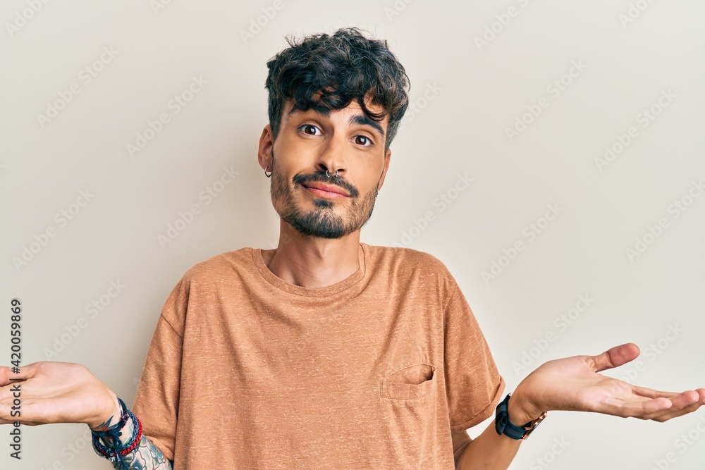 Sticker young hispanic man wearing casual clothes clueless and confused expression with arms and hands raise