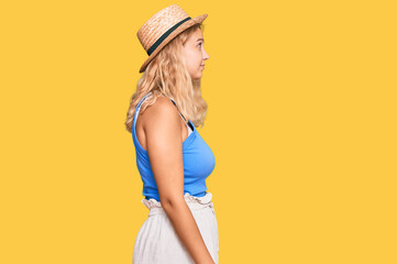 Young blonde girl wearing summer hat looking to side, relax profile pose with natural face with confident smile.