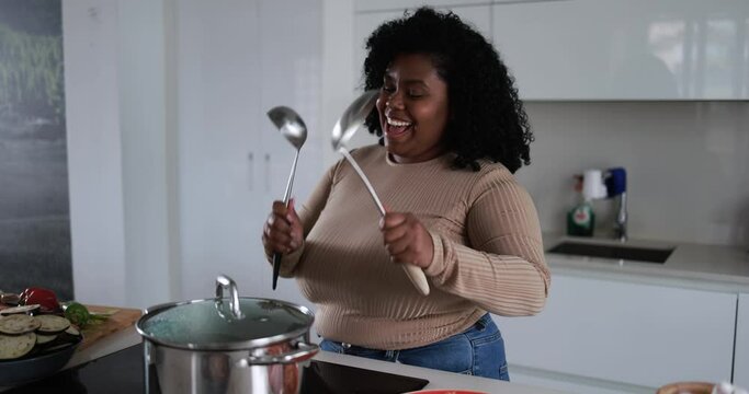 Young curvy latin woman having fun cooking and dacing inside kitchen at home 