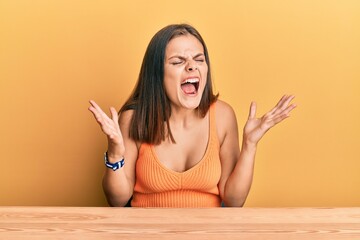 Young caucasian woman wearing casual clothes sitting on the table celebrating mad and crazy for...
