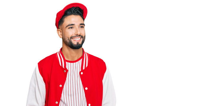 Young man with beard wearing baseball uniform looking away to side with smile on face, natural expression. laughing confident.