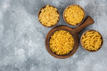 Wooden bowl of raw various pasta on marble background