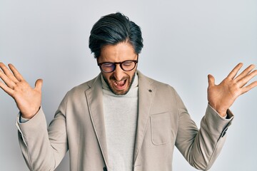 Young hispanic man wearing business jacket and glasses celebrating mad and crazy for success with...