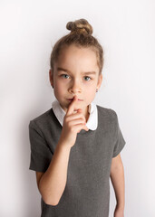 Attractive little girl in a strict school dress, stands on a white background with empty copy space, gestures with her hands, admires a happy expression on her face