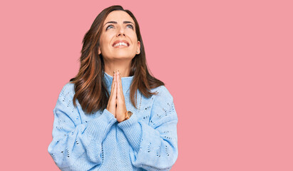 Fototapeta premium Young brunette woman wearing casual winter sweater begging and praying with hands together with hope expression on face very emotional and worried. begging.