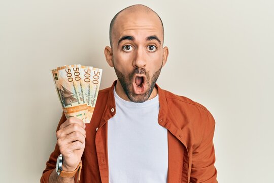 Young hispanic man holding 500 norwegian krone banknotes scared and amazed with open mouth for surprise, disbelief face